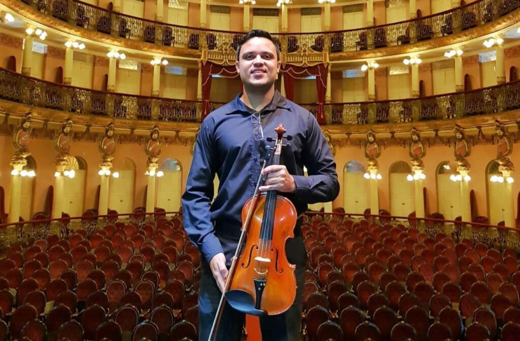Alex Teixeira, idealizador do Projeto Muzikinhas, em teatro de Manaus com instrumento de cordas utilizado nas apresentações educativas para escolas públicas.